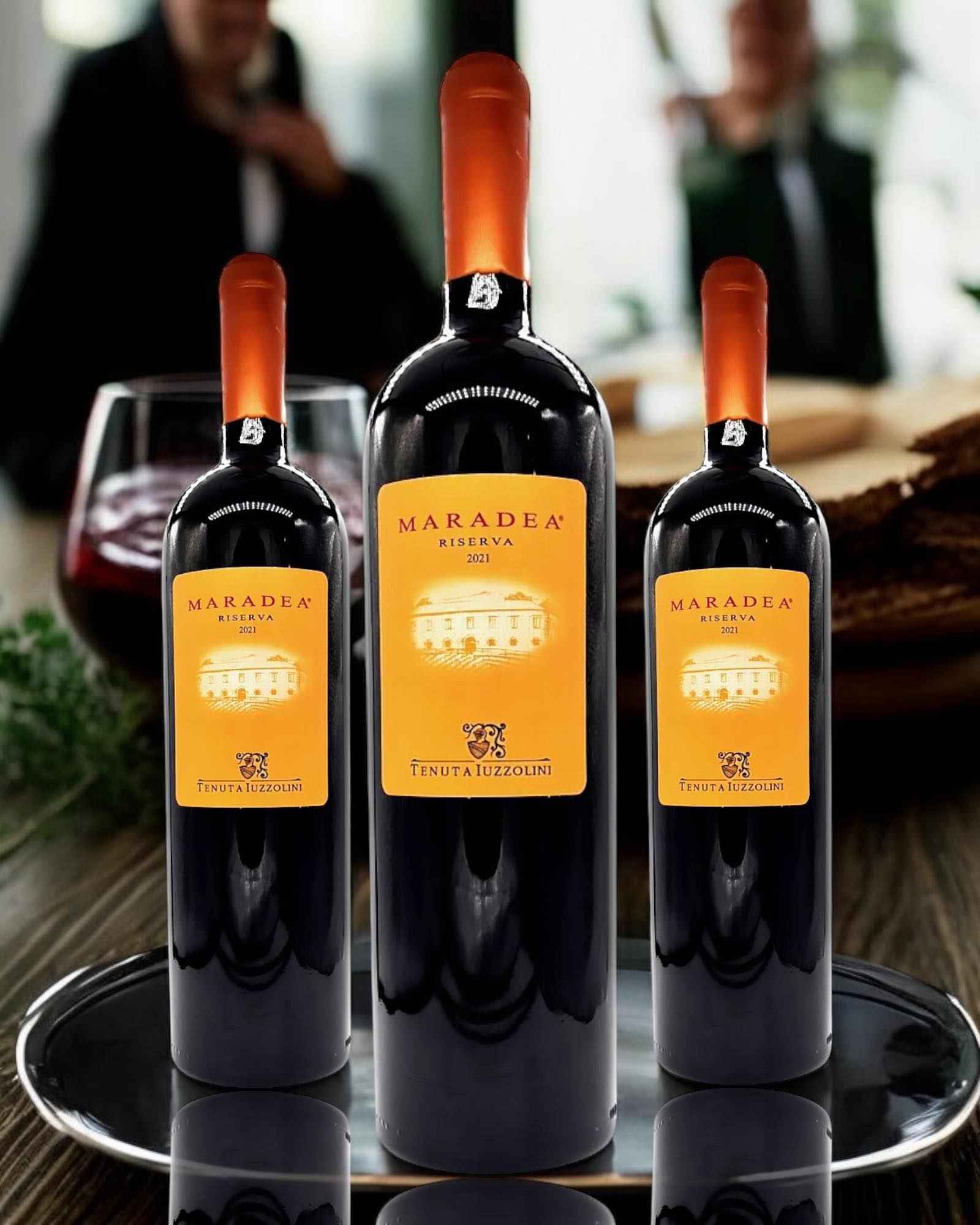 Drei Flaschen Maradea Tenuta Iuzzolini Cirò Riserva DOC 2021 – italienischer Rotwein in verschiedenen Größen auf Tablett mit Weinglas im Hintergrund