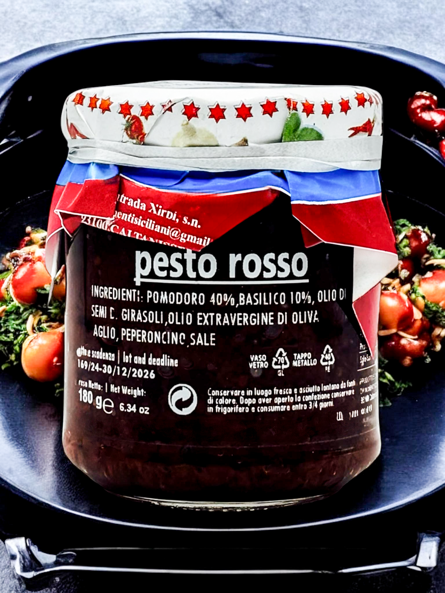Italienisches Pesto Rosso im Glas – aromatische rote Pestosauce aus sonnengetrockneten Tomaten, Basilikum und Olivenöl, präsentiert mit frischen Kirschtomaten auf dunklem Teller