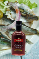 Callipo Colatura di Alici – 250ml Flasche mit traditioneller italienischer Anchovis-Würzsauce, ideal für Pasta und mediterrane Gerichte. Hintergrund mit frischen Sardellen und Zwiebeln.