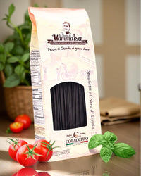 Spaghetti al Nero di Seppia von Mamma Isa in eleganter Verpackung mit Tomaten, Basilikum und mediterranem Hintergrund