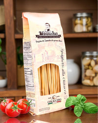 Italienische Spaghetti alla Chitarra von Mamma Isa in dekorativer Verpackung mit Tomaten, Basilikum und eingelegtem Gemüse im Hintergrund