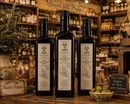 Drei Flaschen Olia Olivenöl Extra Vergine in einer italienischen Feinkostboutique mit mediterraner Atmosphäre
