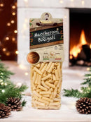 Ein Paket Maccheroni Birigati Pasta (500g) von MammaSicura, dekorativ vor einem gemütlichen Kamin und einer weihnachtlichen Kulisse mit Tannenzweigen und Zapfen präsentiert.