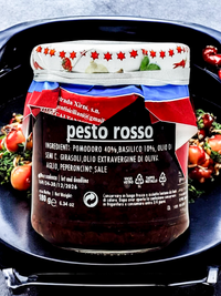Italienisches Pesto Rosso im Glas – aromatische rote Pestosauce aus sonnengetrockneten Tomaten, Basilikum und Olivenöl, präsentiert mit frischen Kirschtomaten auf dunklem Teller

