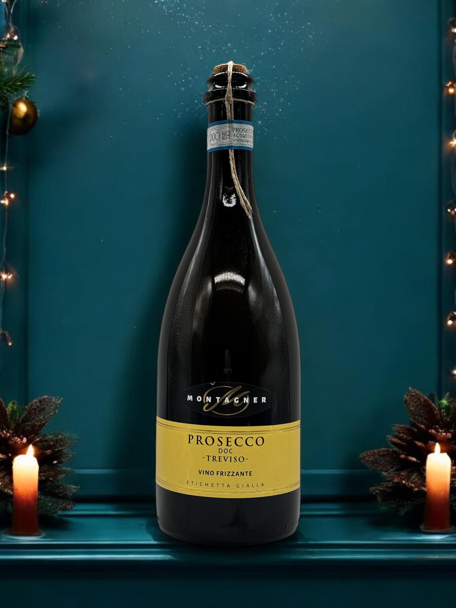 Prosecco Montagner Flasche, weihnachtlich dekoriert mit Kerzen und Tannenzapfen, vor einem blauen festlichen Hintergrund.