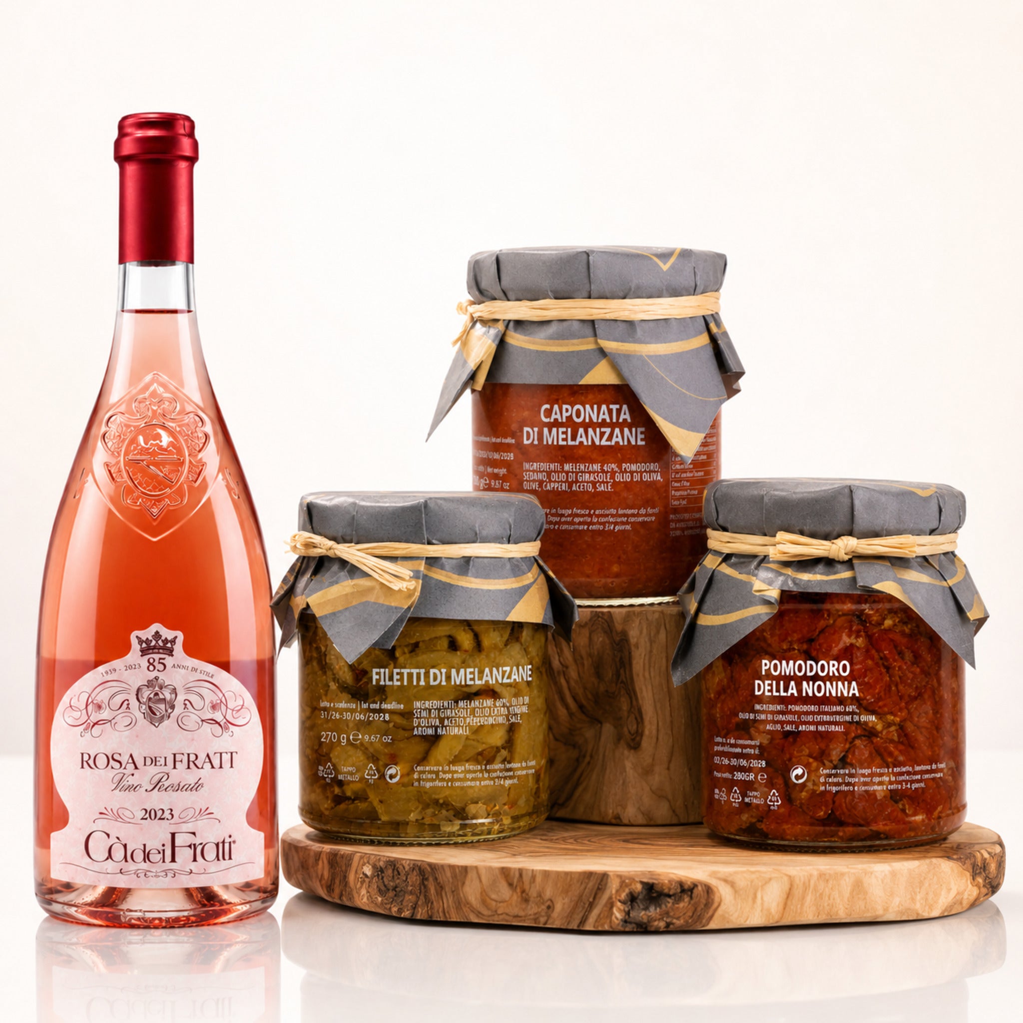 Sizilianisches Aperitivo Paket mit Rosa dei Frati Rosé, Caponata, Filetti di Melanzane und Pomodoro della Nonna auf Holz vor weißem Hintergrund